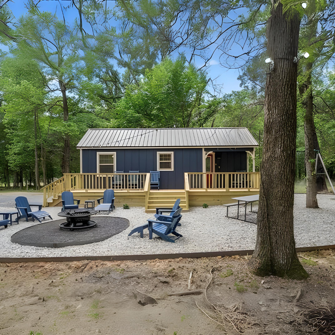 Social posts starting 7924 27 - Lelands Modular Blue cabin with a metal roof on a wooden deck, surrounded by trees, and blue Adirondack chairs around a fire pit.