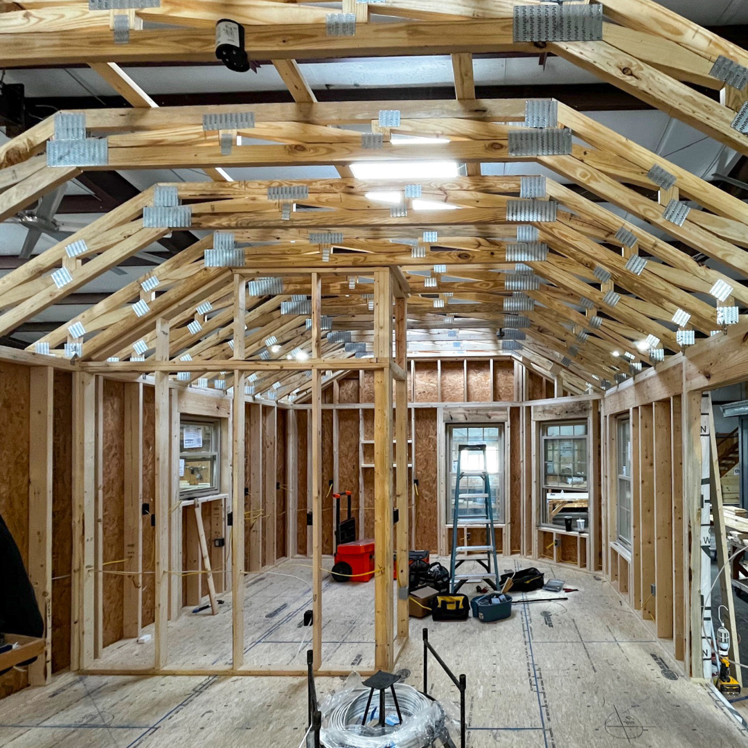 Social posts starting 7924 30 - Lelands Modular Interior of a framed house under construction with exposed roof trusses and metal plates, plywood floors, and scattered tools across the space.